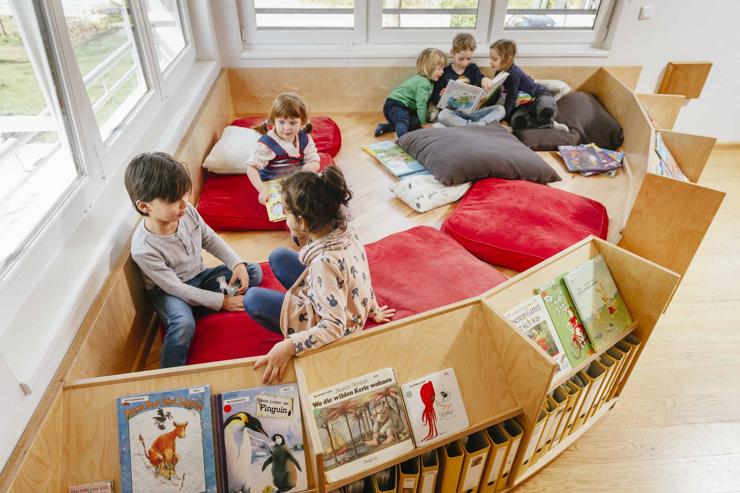 Kinder sitzen in Bücherecke und lesen