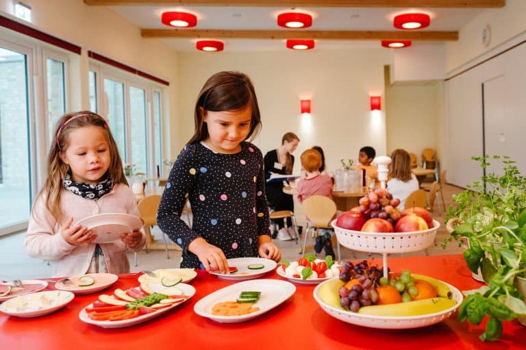 Kinder füllen sich die Teller mit Obst und Gemüse