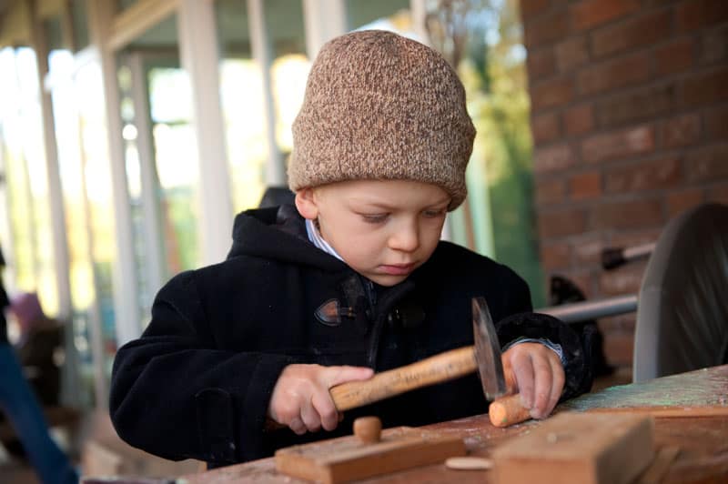 Kind mit Hammer und Holzstück in der Werkstatt
