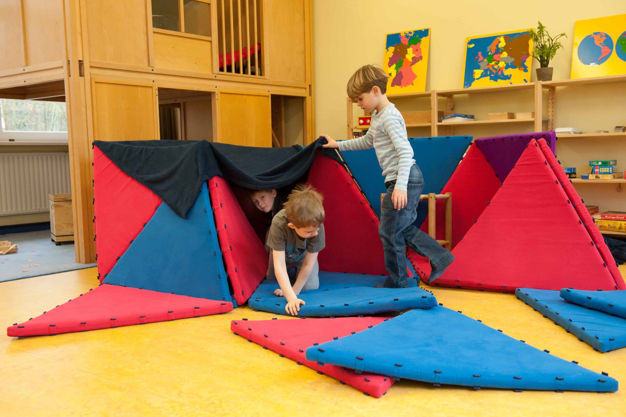 Kinder bauen eine Höhle aus dreieckigen Matten