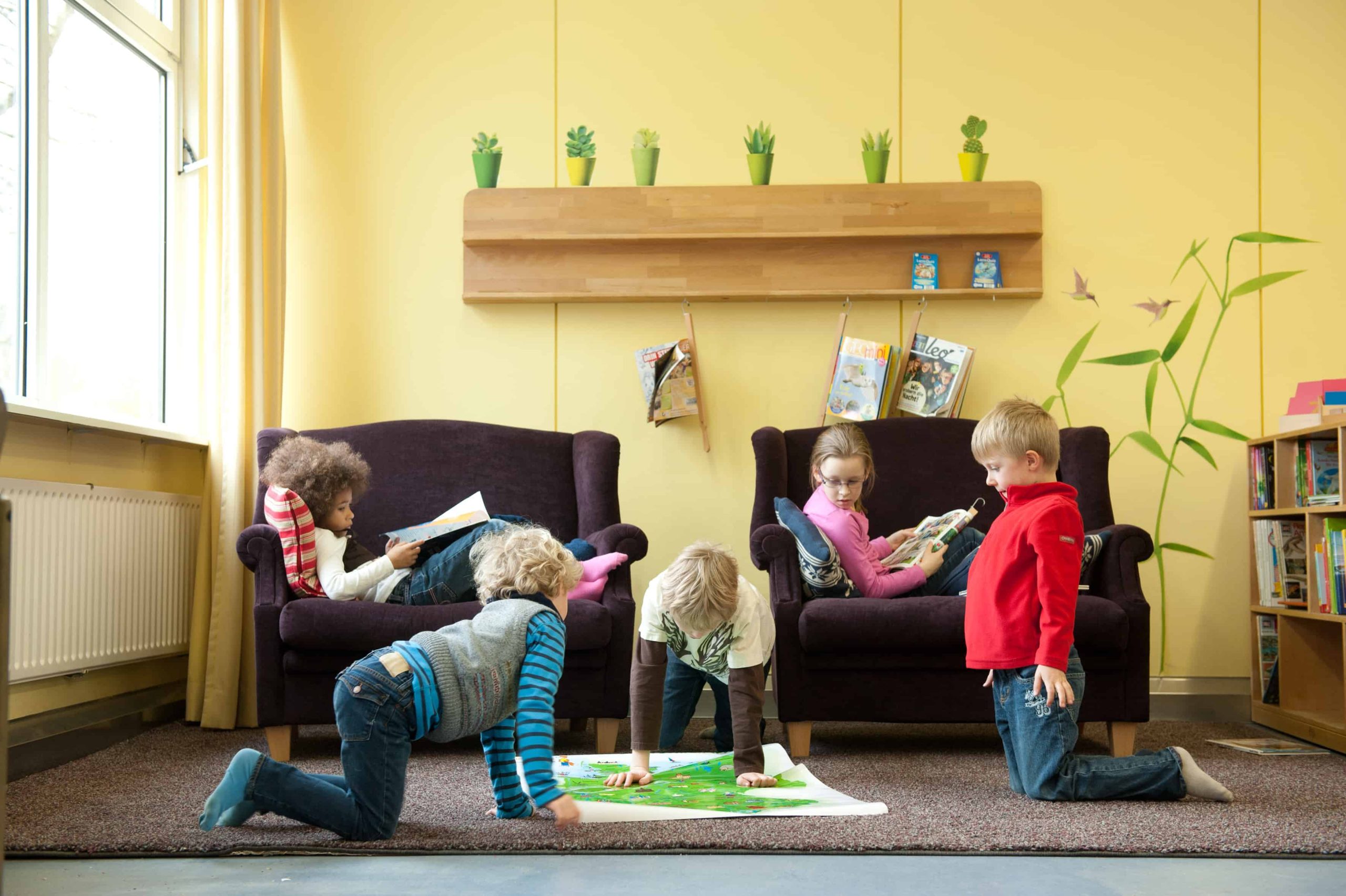 Kinder lesen in Sesseln und andere schauen Weltkarte auf dem Boden an