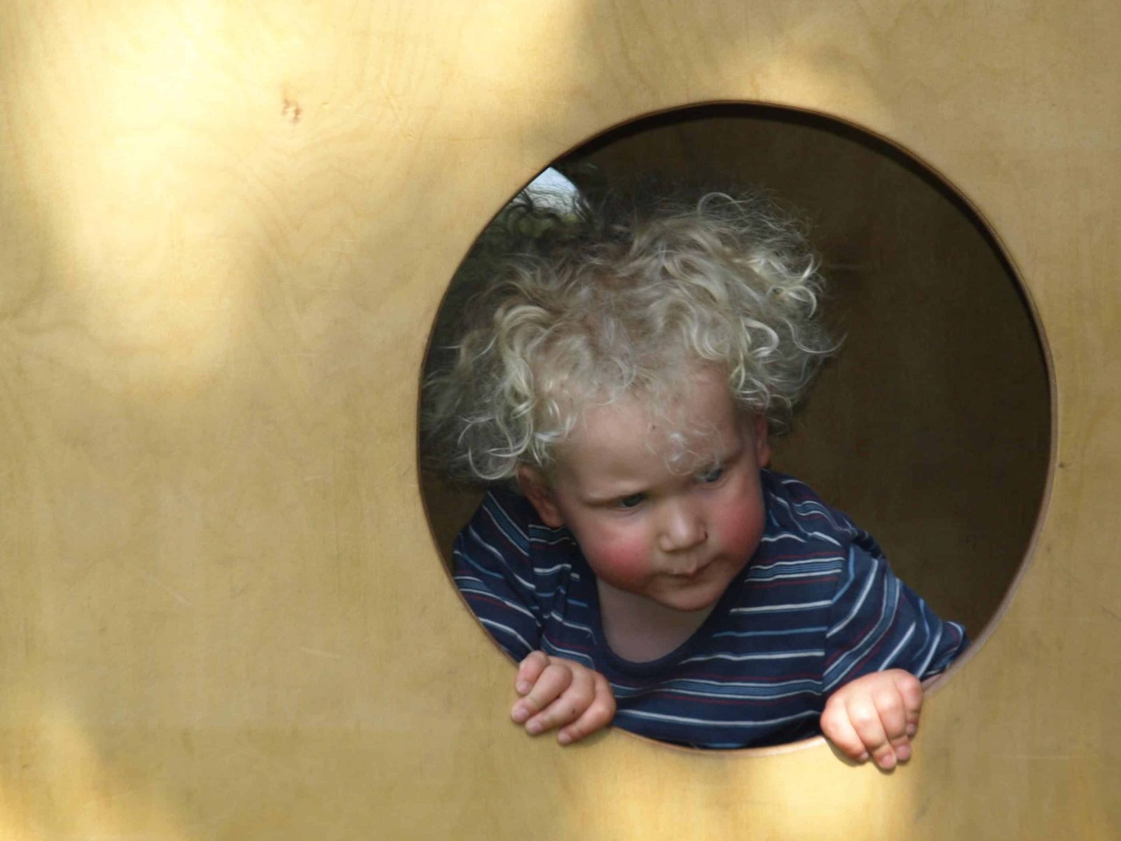 Kind schaut aus einer Holzröhre