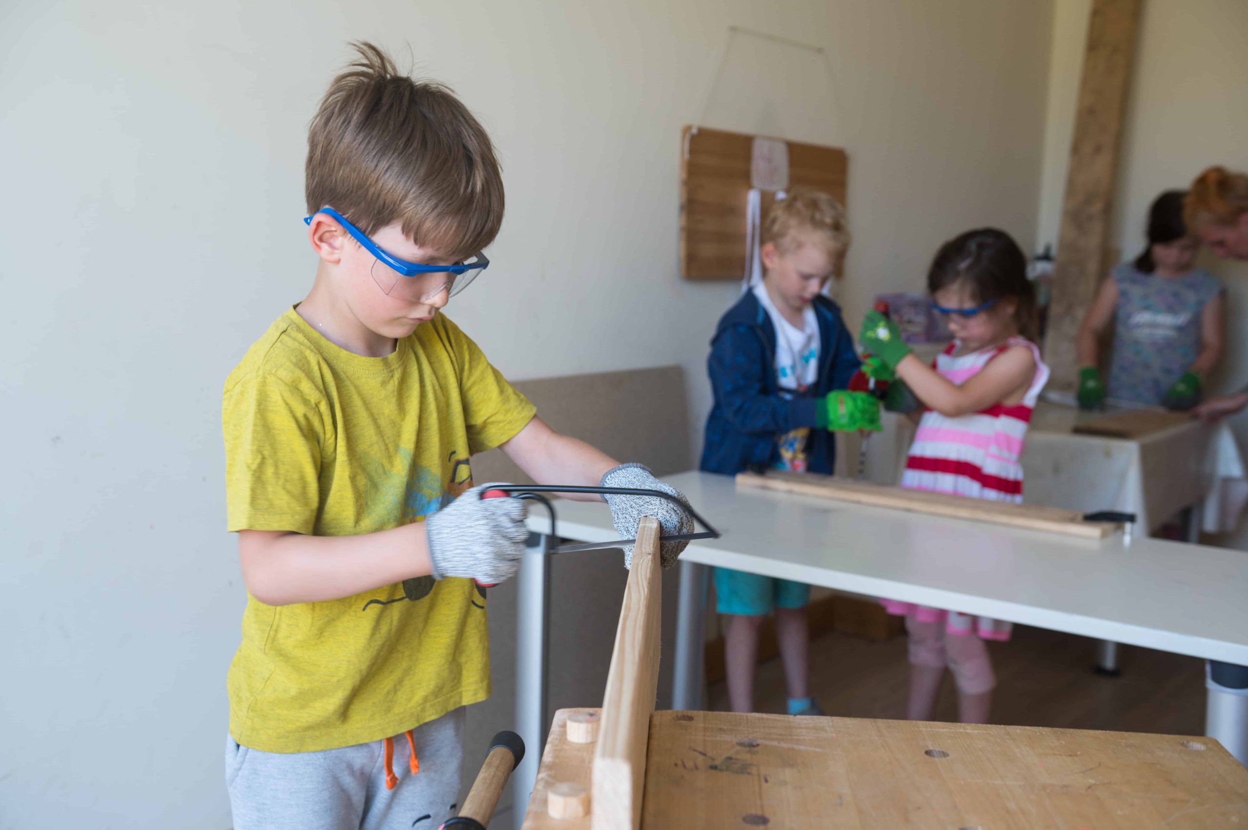 Kinder arbeiten in der Holzwerkstatt mit Säge und Bohrer